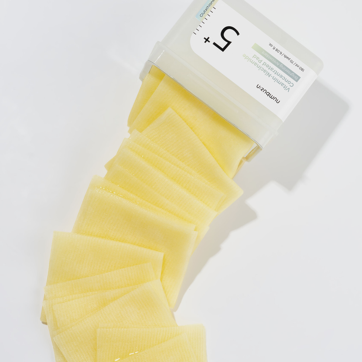 Ein geöffneter Behälter mit numbuzin No.5 Vitamin-Niacinamid-Konzentrat-Pads wird auf einer weißen Fläche aufgefächert.
