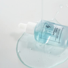 Eine Tropfflasche mit „Numbuzin No. 6 Deep Sleep Mask Serum“ mit blauer Flüssigkeit, die auf eine weiße Oberfläche verschüttet wurde.