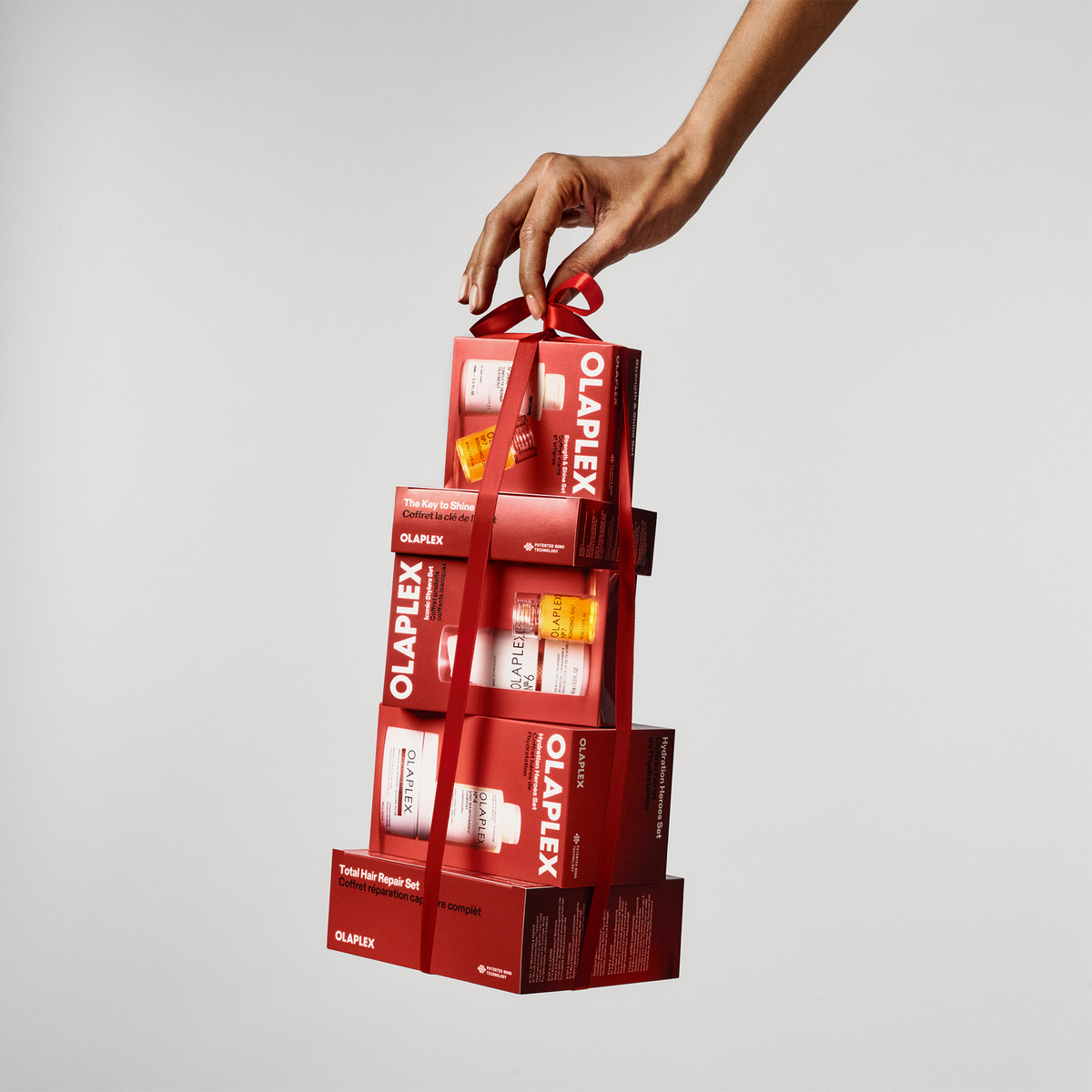 Eine Hand hält einen Stapel aus drei roten Hydration Heroes Holiday Kit 2026-Geschenkboxen, die mit einem roten Band zusammengebunden sind.