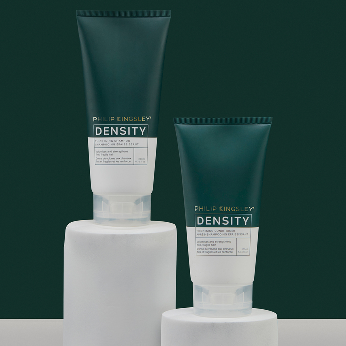 Zwei Tuben „Philip Kingsley Density Thickening Conditioner“ auf weißen Sockeln vor einem dunkelgrünen Hintergrund.