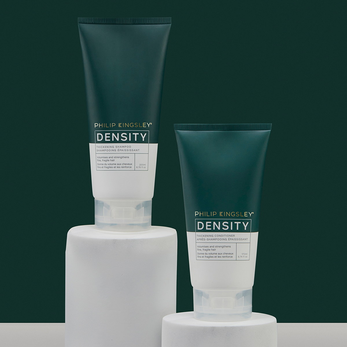 Zwei dunkelgrüne Tuben „Philip Kingsley Density Thickening Shampoo“ auf weißen Sockeln vor einem dunkelgrünen Hintergrund.