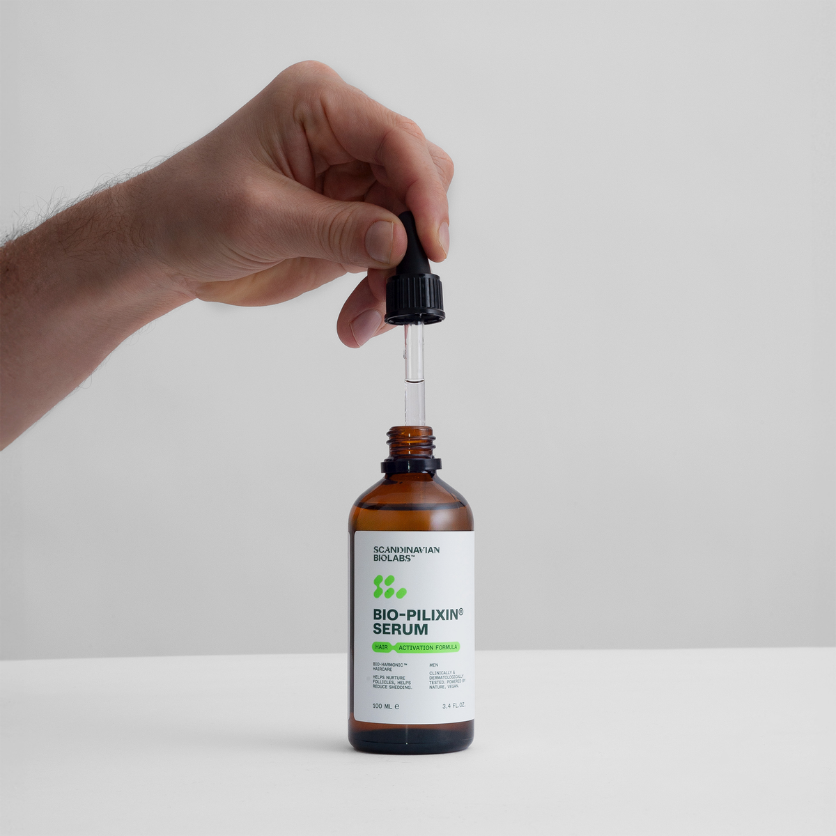 Eine Hand hält einen Tropfer über einer braunen Flasche mit der Aufschrift Bio-Pilixin® Serum von Scandinavian Biolabs, die sich vor einem schlichten Hintergrund befindet.