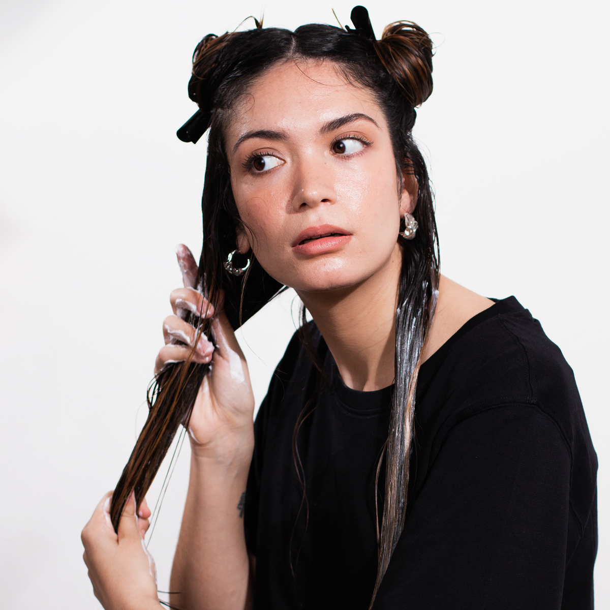 Frau trägt die Scandinavian Biolabs Hair Hydration Mask auf ihr nasses dunkles Haar auf und blickt zur Seite.