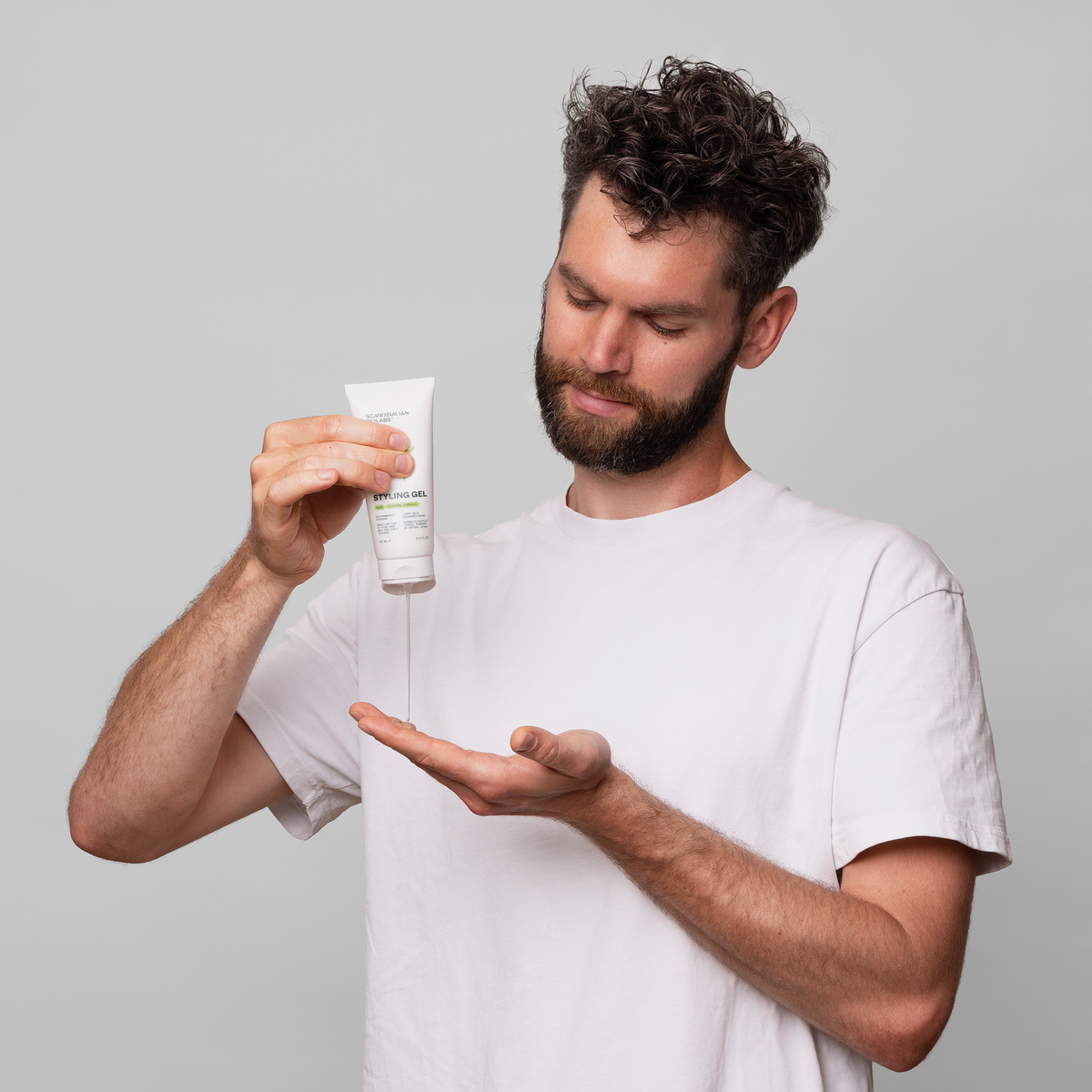 Ein Mann in einem weißen Hemd drückt Scandinavian Biolabs Hair Styling Gel aus einer Tube auf seine Hand vor einem schlichten grauen Hintergrund.
