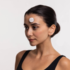 Eine Frau mit dunklem Haar und schwarzem Oberteil trägt das STYLPRO LED Spot & Blemish Patch auf ihrer Stirn vor einem weißen Hintergrund.