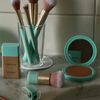 SWEED-Foundation-Pinsel, Puder-Kompakt und Anspitzer auf einer Marmorplatte zusammen mit anderen Make-up-Utensilien.