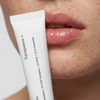 Eine Nahaufnahme von glänzenden Lippen und einer Transparent Lab Lip Renewal Tube, die in die Nähe des Mundes gehalten wird.