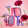 Unbrush und Super Mini Set Neon Pink mit zwei Haarbürsten in Originalgröße und zwei Mini-Haarbürsten in Neonrosa und Lila, umrahmt von passenden Blumen.