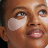 Eine lächelnde Person blickt nach oben und präsentiert in einer Nahaufnahme die unter den Augen aufgetragenen XLASH Awakening Eye Gels.