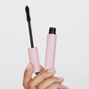 Eine Hand hält die XLASH Lash Hero Mascara, deren Bürste entfernt wurde, aufrecht vor einem weißen Hintergrund.