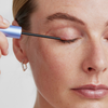 Eine Person trägt das XLASH Xlash Sensitive Wimpernserum mit einem dünnen Pinselapplikator auf das obere Augenlid auf.