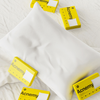 Ein weißes Kissen mit Acnemy Antibakterieller Kopfkissenbezug, umgeben von gelben Acnemy Boxen auf einem weißen Bett.