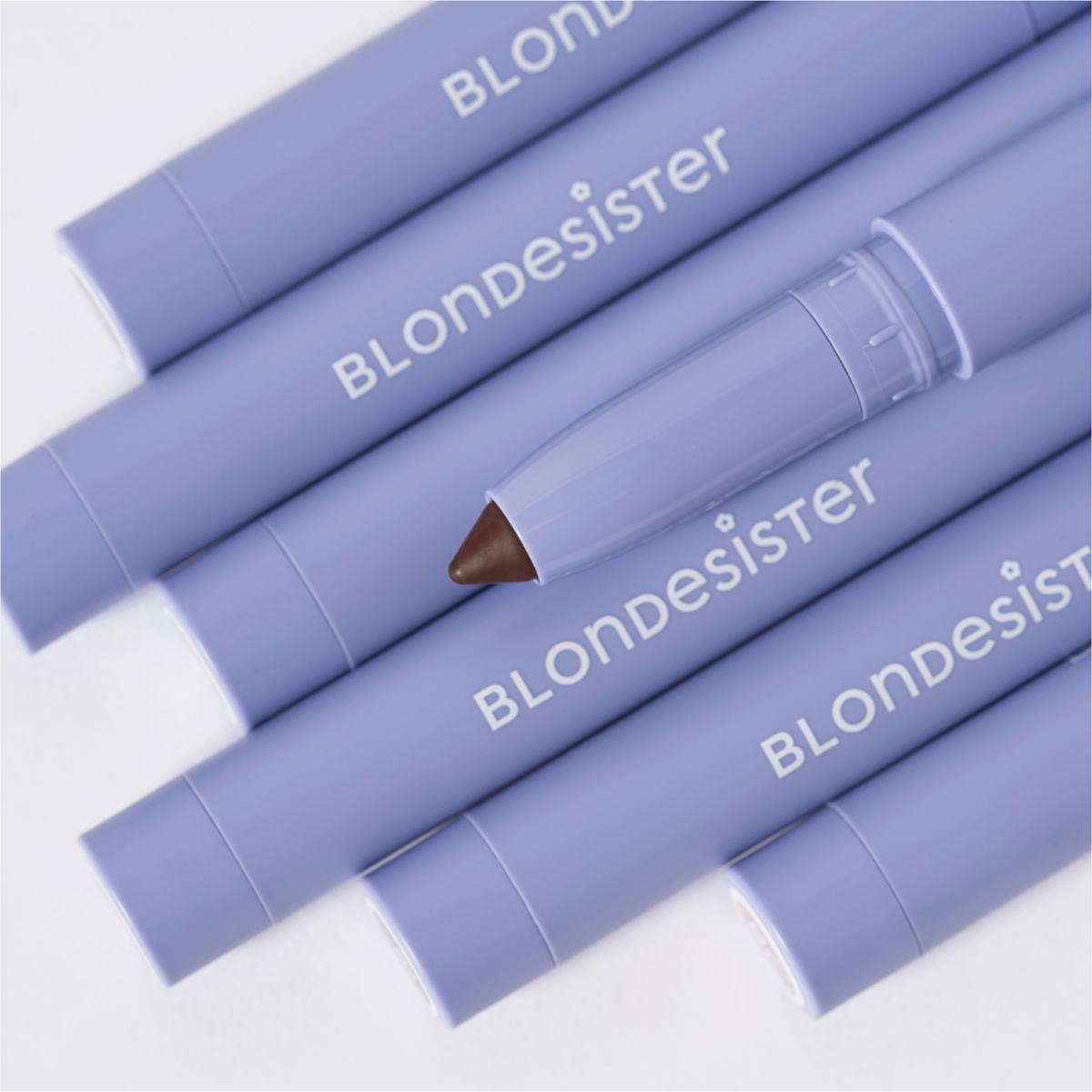Sechs lavendelfarbene BLONDESISTER 3-IN-1-EYES-ON-ME-Stifte stehen in einer Reihe, einer davon ist geöffnet und gibt den Blick auf eine braune Spitze frei.