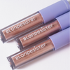Drei Tuben „BLONDESISTER GLOWEYE EYESHADOW“ mit hellvioletten Verschlusskappen, die diagonal auf einer weißen Fläche angeordnet sind.