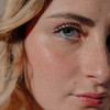 Nahaufnahme einer Frau, die den Lidschatten „BLONDESISTER GLOWEYE“ trägt: blaue Augen, Sommersprossen, glänzende Lippen, natürliches Make-up im Sonnenlicht.