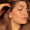 Eine Frau mit langen braunen Haaren trägt den „BLONDESISTER READY TO GLOW HIGHLIGHTER“ in der Farbe „Crystal Mood 01“ und strahlt mit geschlossenen Augen im Sonnenlicht.