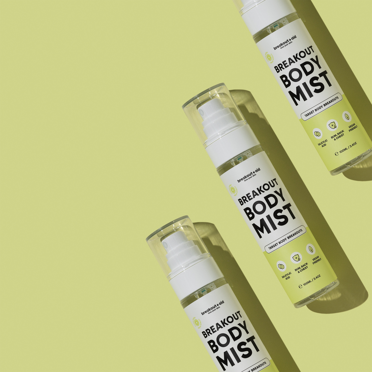 Drei Flaschen Breakout Body Mist, diagonal auf einem hellgelben Hintergrund angeordnet.