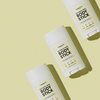 Drei Breakout+Aid Glycolic Acid Body Stick-Hautpflegeprodukte, diagonal auf einem hellgelben Hintergrund angeordnet.