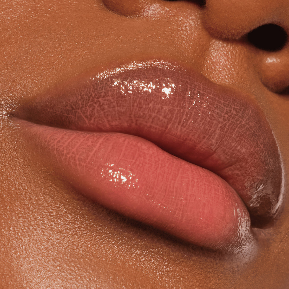 Nahaufnahme von glänzenden, rosafarbenen Lippen auf glatter brauner Haut, die Colour Cushion Juicy Lip Oil von Catrice Cosmetics tragen.