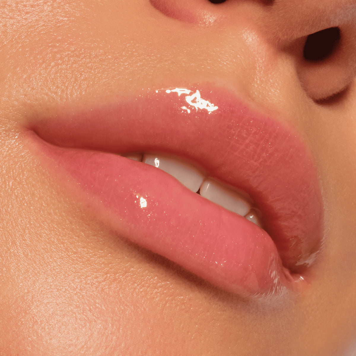 Nahaufnahme von glänzenden, rosafarbenen Lippen mit glatter Haut und leicht sichtbaren Zähnen, die Catrice Cosmetics Colour Cushion Juicy Lip Oil tragen.