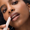 Eine Frau trägt den Catrice Cosmetics Diamond Glaze Gloss Stick auf ihre Lippen auf, wobei eine Nahaufnahme ihr Gesicht und ihr Make-up hervorhebt.