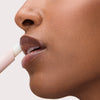 Seitliche Nahaufnahme von Lippen, auf die ein transparenter Gloss-Stick aufgetragen wird, für ein glänzendes, pflegendes Finish.