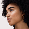 Nahaufnahme eines Gesichts mit natürlichem Make-up und dezentem Highlighter-Schimmer auf den Wangenknochen, goldene Ohrringe im Ohr.