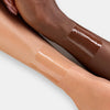 Zwei Unterarme mit unterschiedlichen Hauttönen, beide mit einem aufgetragenen, glänzenden Swatch einer Lippenmaske oder eines Glosses.
