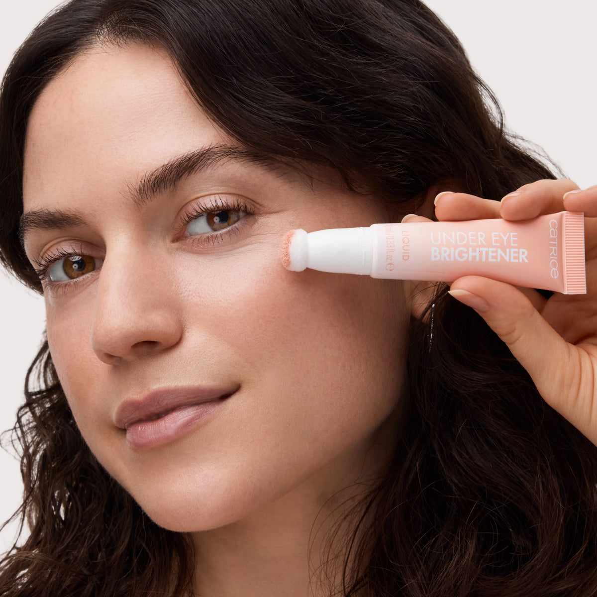 Eine Frau trägt den Catrice Cosmetics Under Eye Brightener Liquid mit einer Applikatortube auf die Haut unter ihrem Auge auf.