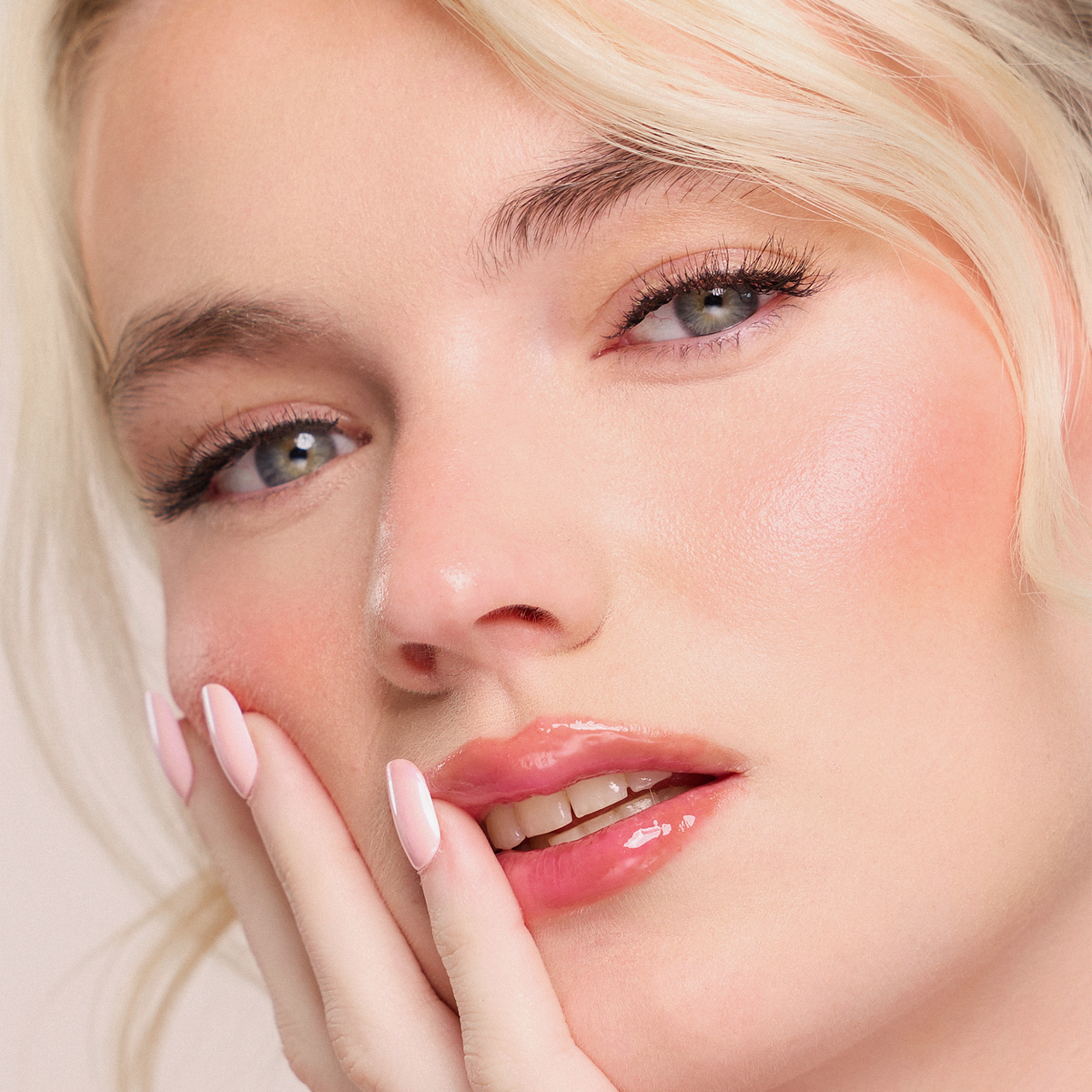 Nahaufnahme einer Frau mit taufrischer Haut und zartem Rouge, die Dominique Cosmetics Juicy Lip Balm und hellrosa manikürte Nägel trägt.