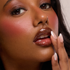 Nahaufnahme einer Frau mit glänzenden Lippen, die Dominique Cosmetics Juicy Lip Balm, schimmernden Lidschatten, Rouge und manikürte Nägel trägt.