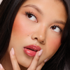 Eine Frau mit glänzenden Lippen trägt Juicy Lip Balm von Dominique Cosmetics und berührt ihr Gesicht mit manikürten Fingern.