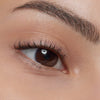 Eine Nahaufnahme eines braunen Auges mit langen Wimpern, die durch die Essence curl FIXING Lash Base verstärkt werden.