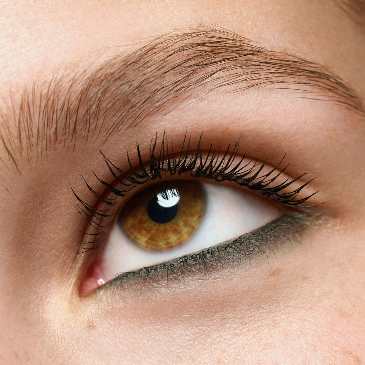 Nahaufnahme eines Auges mit olivgrünem Eyeliner am unteren Wimpernkranz, die Wimpern sind getuscht und das Auge wirkt wach und betont.