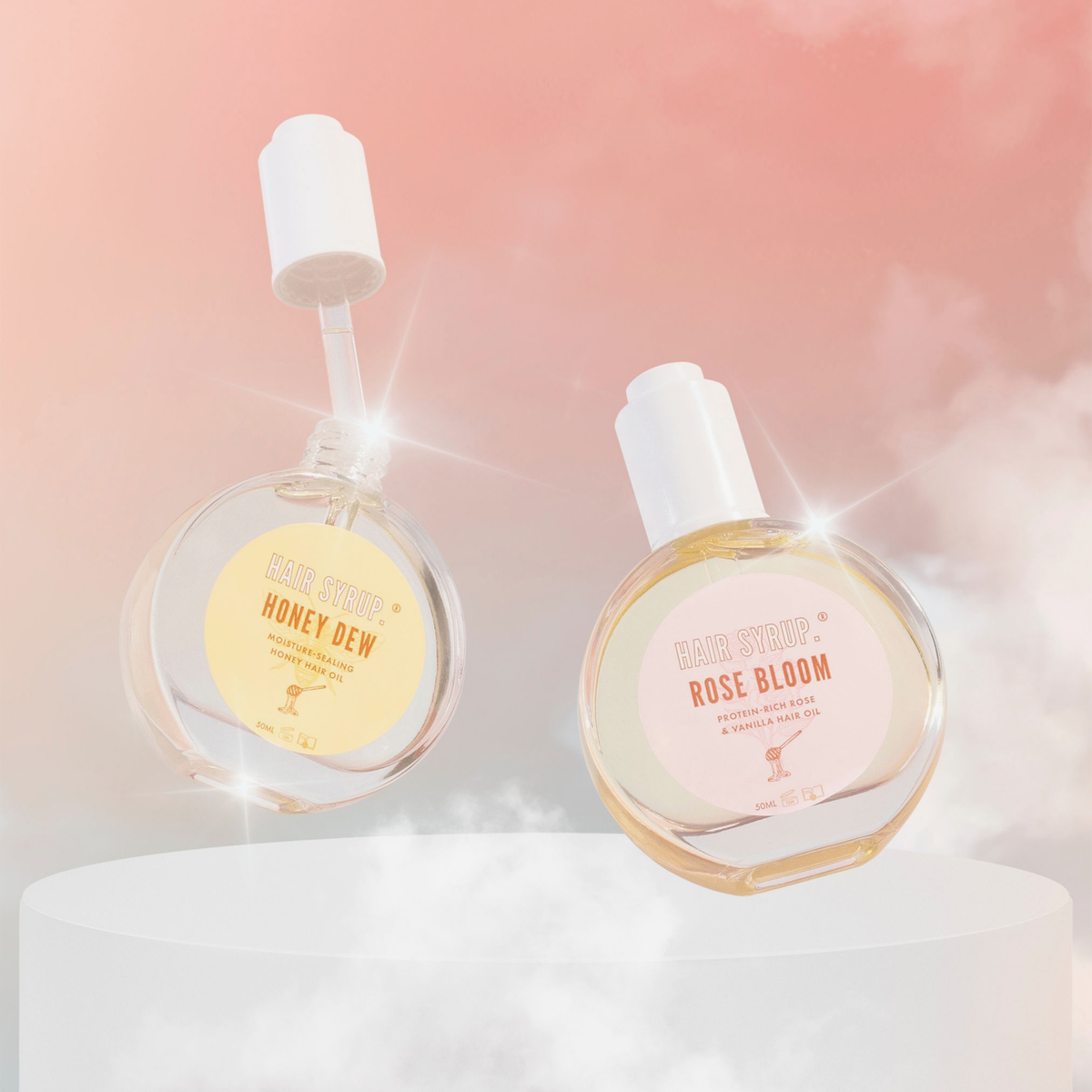 Zwei schwebende Hair-Syrup-Haaröle, Honey Dew und Rose Bloom, vor rosigem Himmel; Glasflaschen glänzen, Etiketten sichtbar.