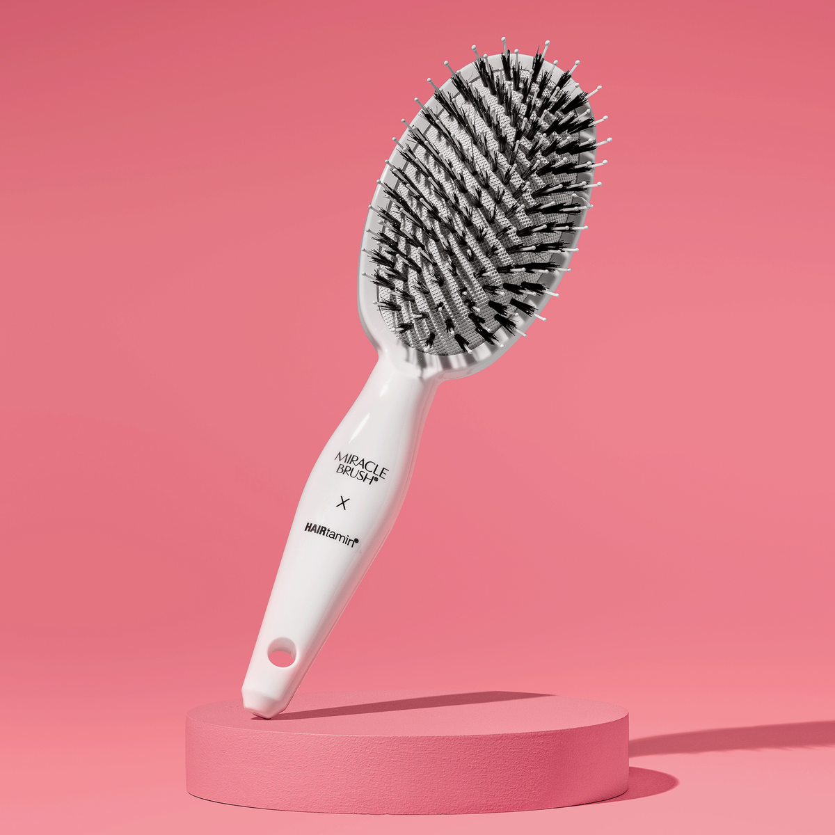 Weiße Miracle Brush x Hairtamin Haarbürste mit gemischten Borsten, freigestellt auf rosafarbenem Hintergrund.