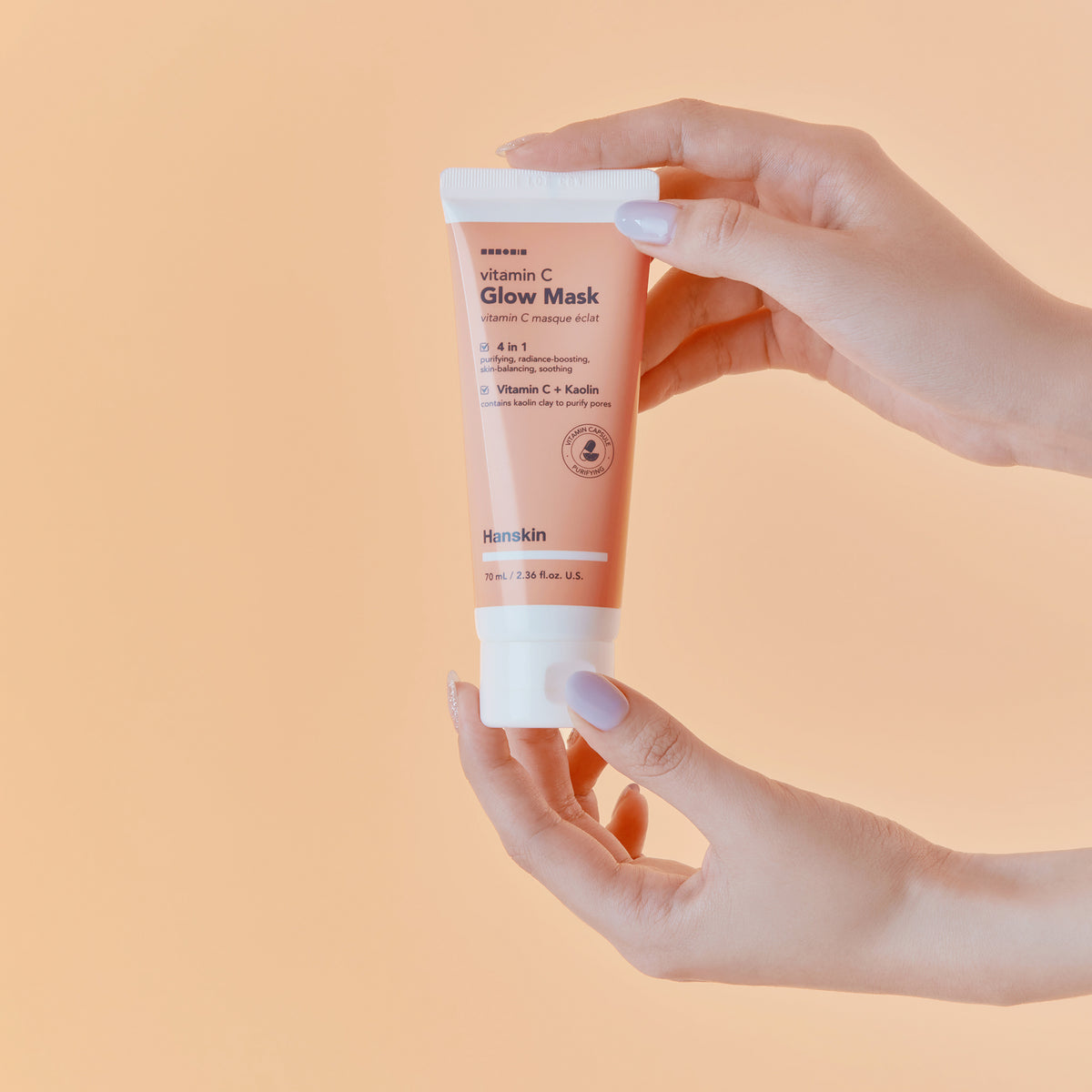 Hände halten Hanskin Vitamin C Glow Mask vor pfirsichfarbenem Hintergrund.