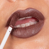 Nahaufnahme einer Person, die den „Over The Garden Wall Rock Fact Velvet Liquid Lipstick“ von Lethal Cosmetics mit einem weißen Applikator aufträgt.