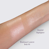 Auf einem Arm sind zwei schimmernde Farbmuster zu sehen: der „Pottsfield Highlighter“ und das „Woodsman’s Lantern Shimmering Body Oil“ von Lethal Cosmetics.