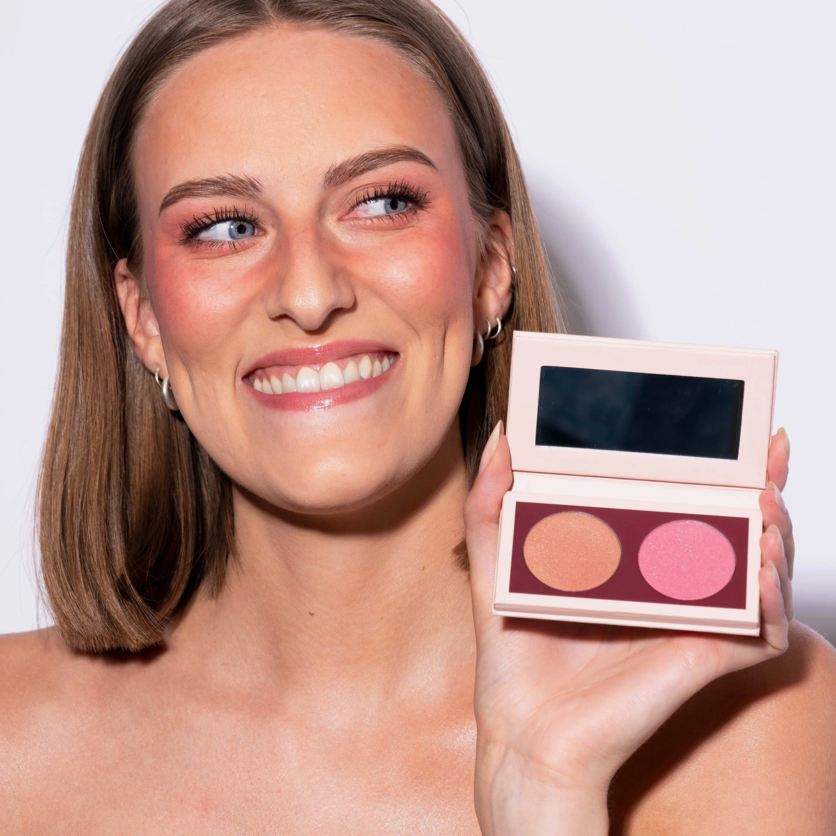 Eine Frau mit dunkelblondem Bob hält die LH Cosmetics Duo Dimension Charming und lächelt.