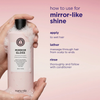 Eine Hand hält eine rosa Flasche „Maria Nila Mirror Gloss Shampoo“ in der Hand; die Gebrauchsanweisung ist auf einem passend rosa Hintergrund zu sehen.