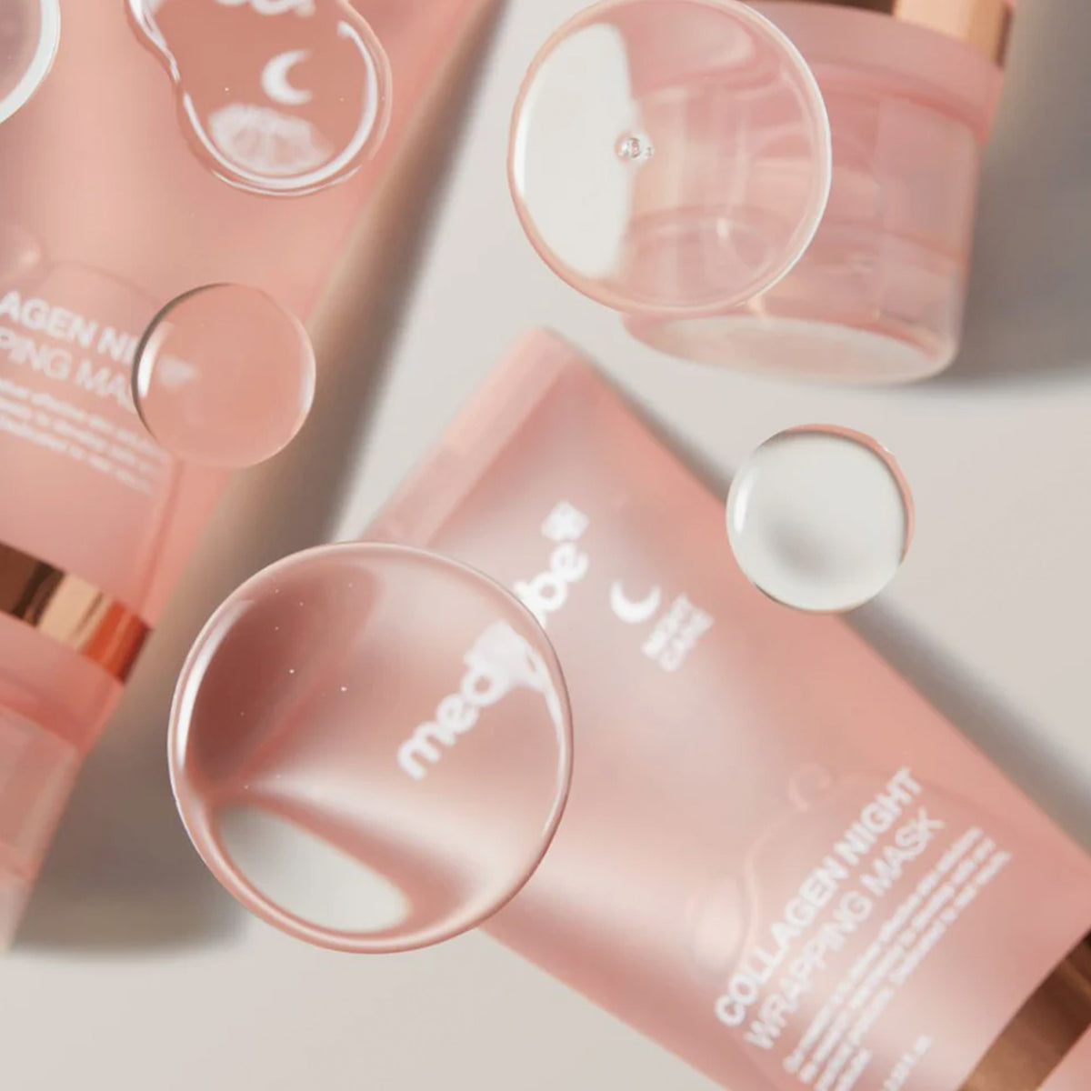 Mehrere rosa Tuben der Medicube Collagen Night Wrapping Mask mit schwebenden Tropfen auf hellem Hintergrund.