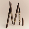 Vier NABLA Cosmetics Freckle Maker Pens, braun und gold, einer ohne Kappe, auf beigefarbenem Hintergrund.