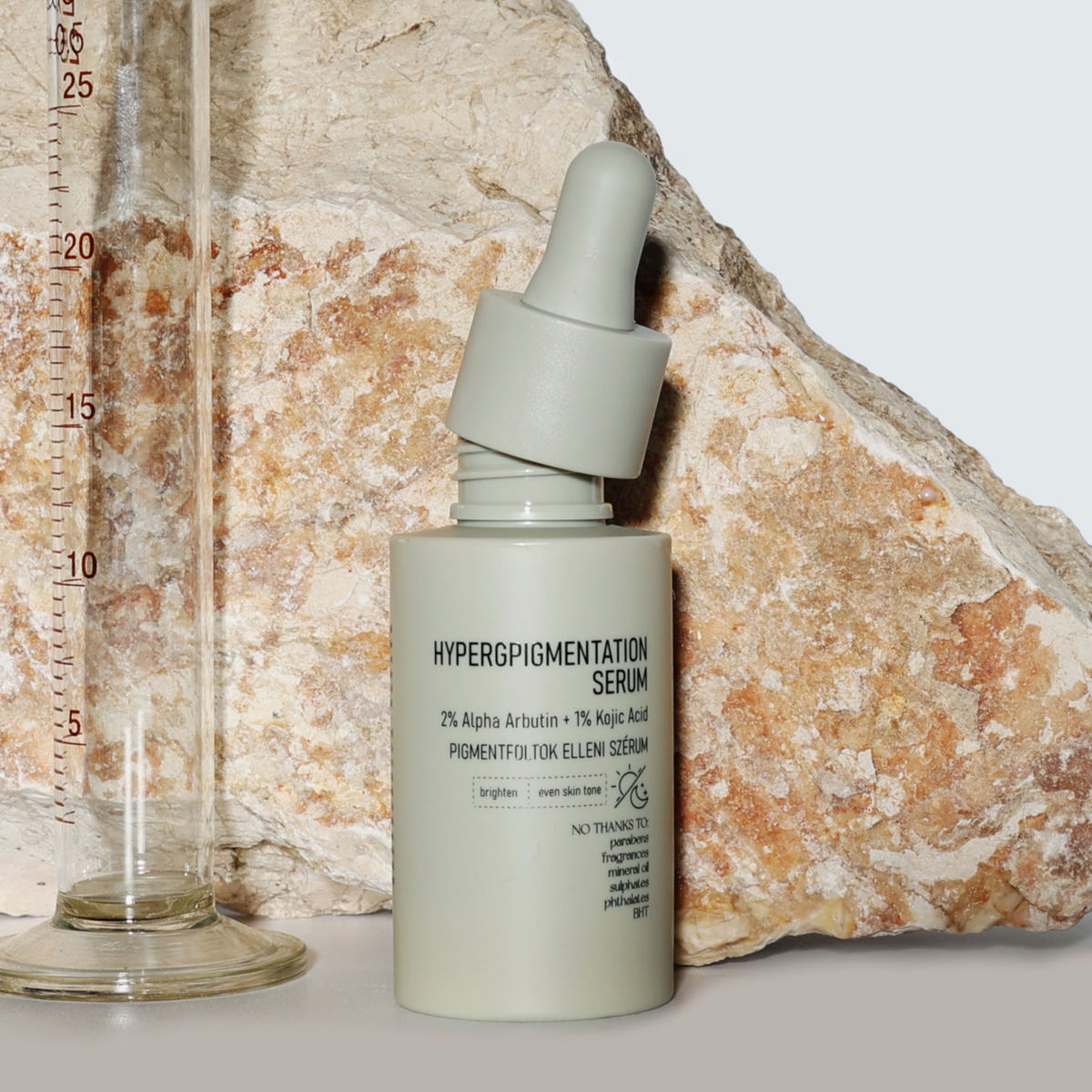 Eine Flasche NERDS. Hyperpigmentation Serum mit einer Pipette ist vor einem Stein und einem Glasmesszylinder ausgestellt.