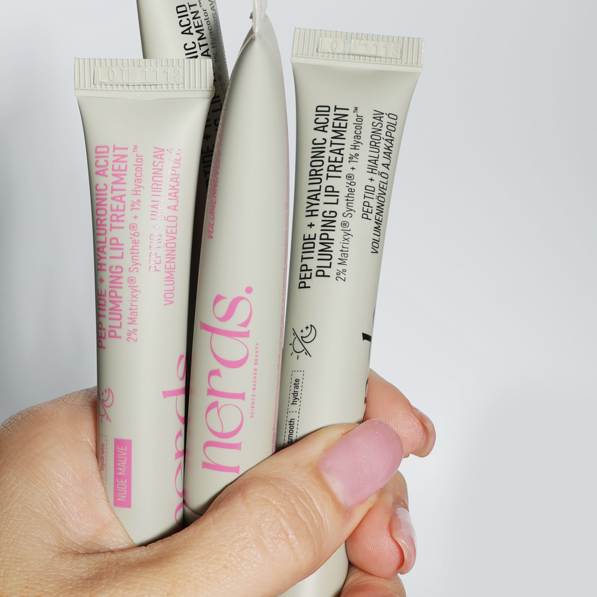 Eine Hand hält mehrere Tuben NERDS. Peptid + Hyaluronsäure Lippenbehandlung.