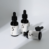 Drei schwarze Fläschchen mit numbuzin No.5+ Vitamin-Konzentrat-Serum; zwei aufrecht und eines liegend mit abgenommenem Tropfer.