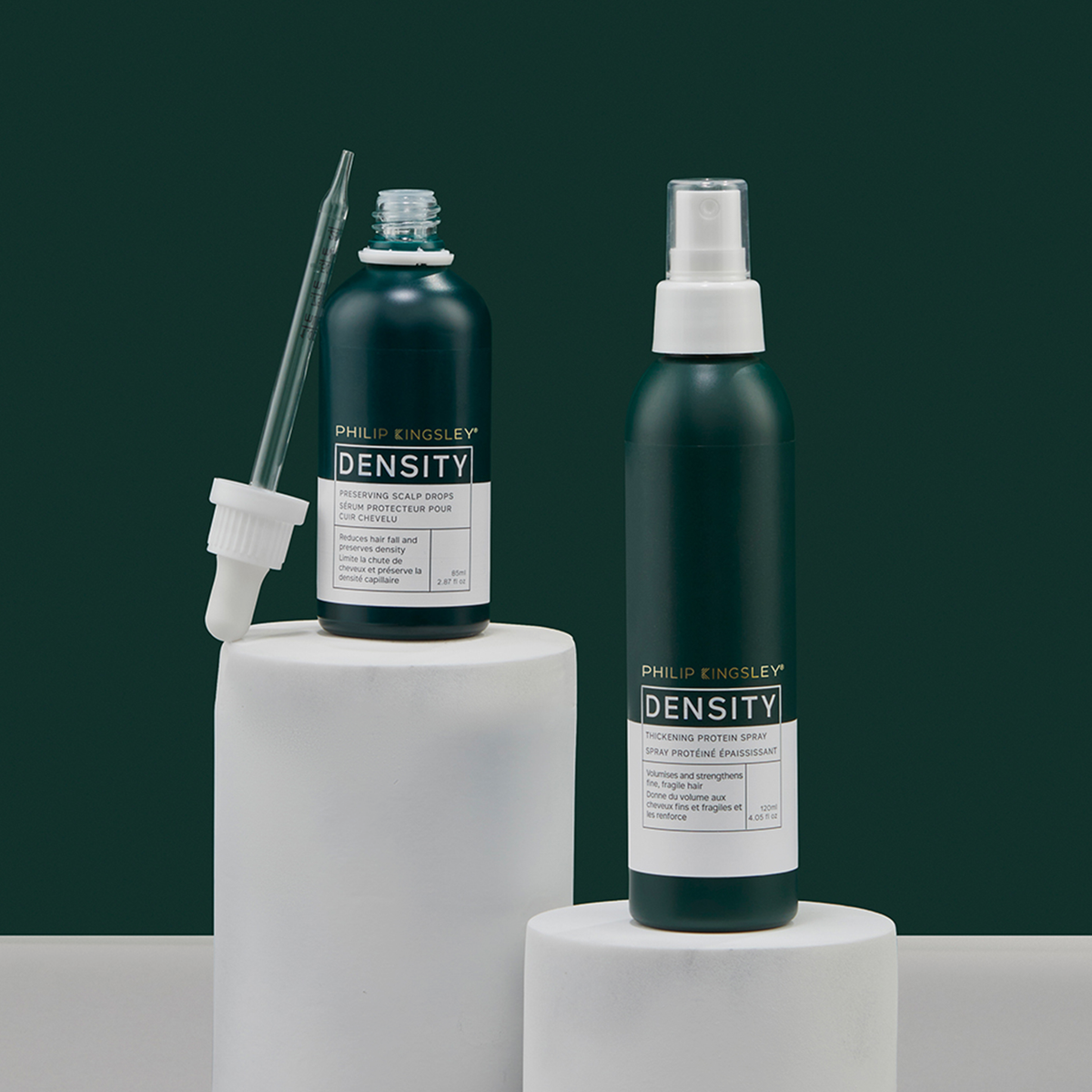 Zwei Flaschen „Philip Kingsley Density Thickening Protein Spray“ auf weißen Sockeln: eine Tropfflasche und eine Sprühflasche, beide mit weißen Etiketten.