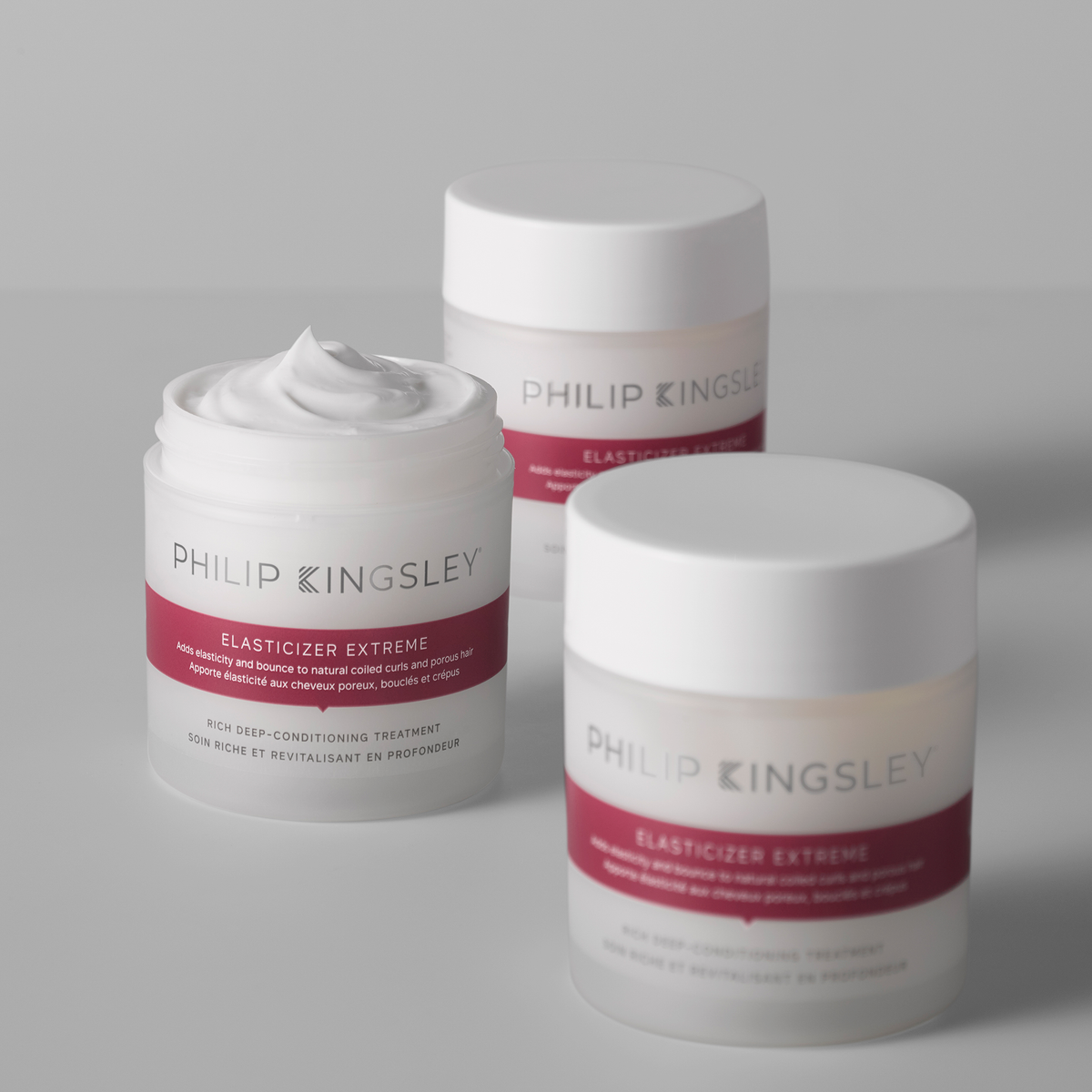 Drei Tiegel „Philip Kingsley Elasticizer Extreme“ – einer geöffnet, aus dem die cremige Pflege zu sehen ist, zwei geschlossen – auf einer weißen Fläche.