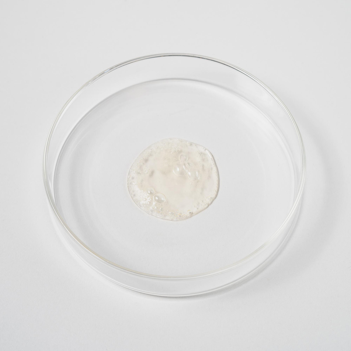 Eine durchsichtige Petrischale mit einer kleinen Menge Bio-Pilixin® Shampoo+ Men von Scandinavian Biolabs, die in der Mitte eine durchscheinende gelartige Substanz auf weißem Hintergrund zeigt.