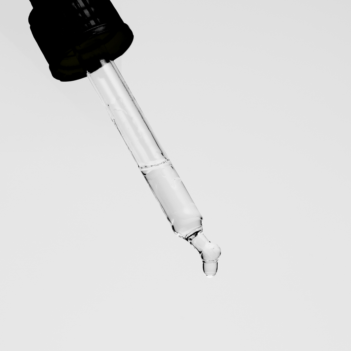 Glaspipette mit transparentem Serum und fallendem Tropfen vor hellem Hintergrund.